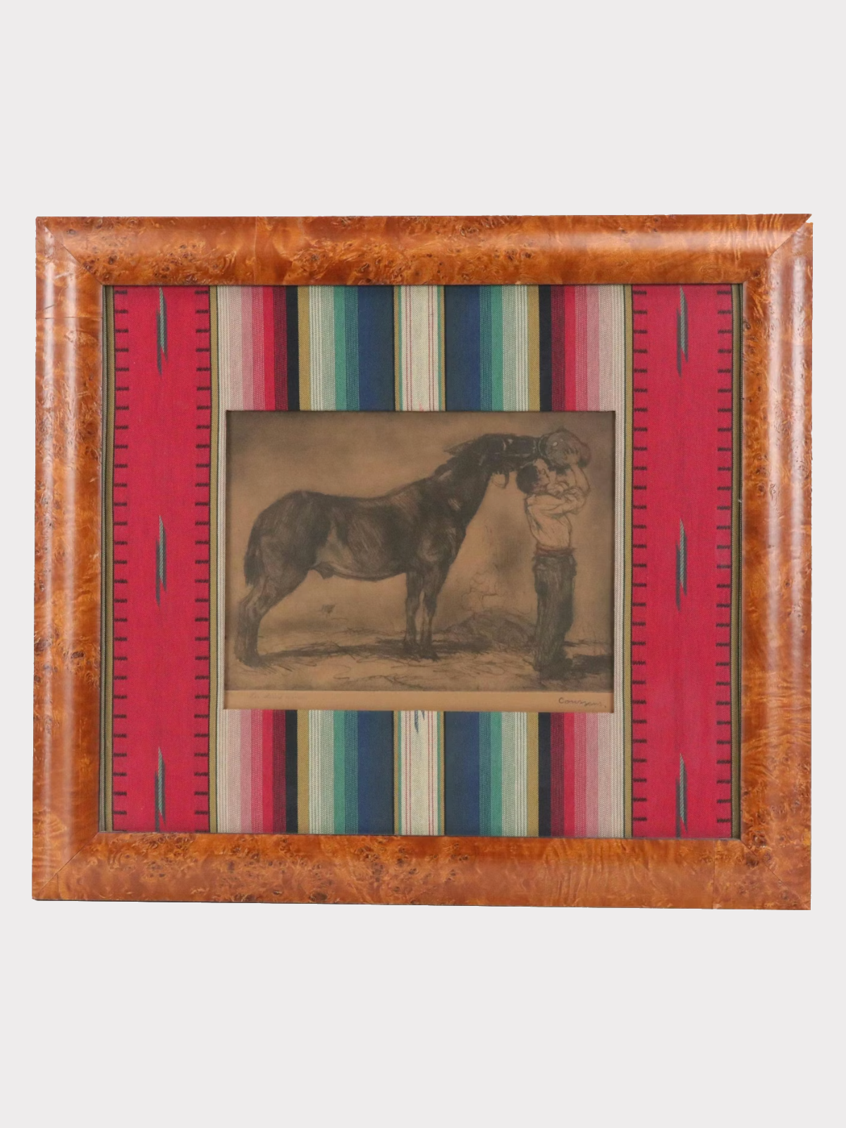An etching of a person feeding a horse, titled 'Les Deux Amis,' framed in a burl wood frame with a woven mat, on a striped background.